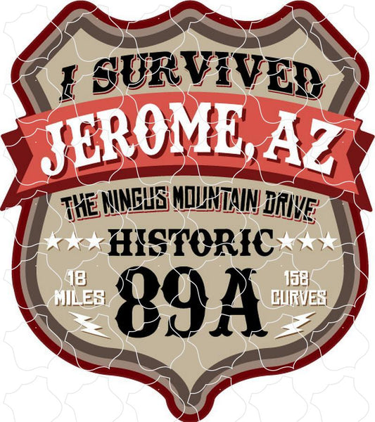 A brown shield with the text 'I Survived The Mingus Mountain Drive Historic 89A 18 Miles 158 Curves' in black, featuring a red banner across the center with 'Jerome, AZ' in white.